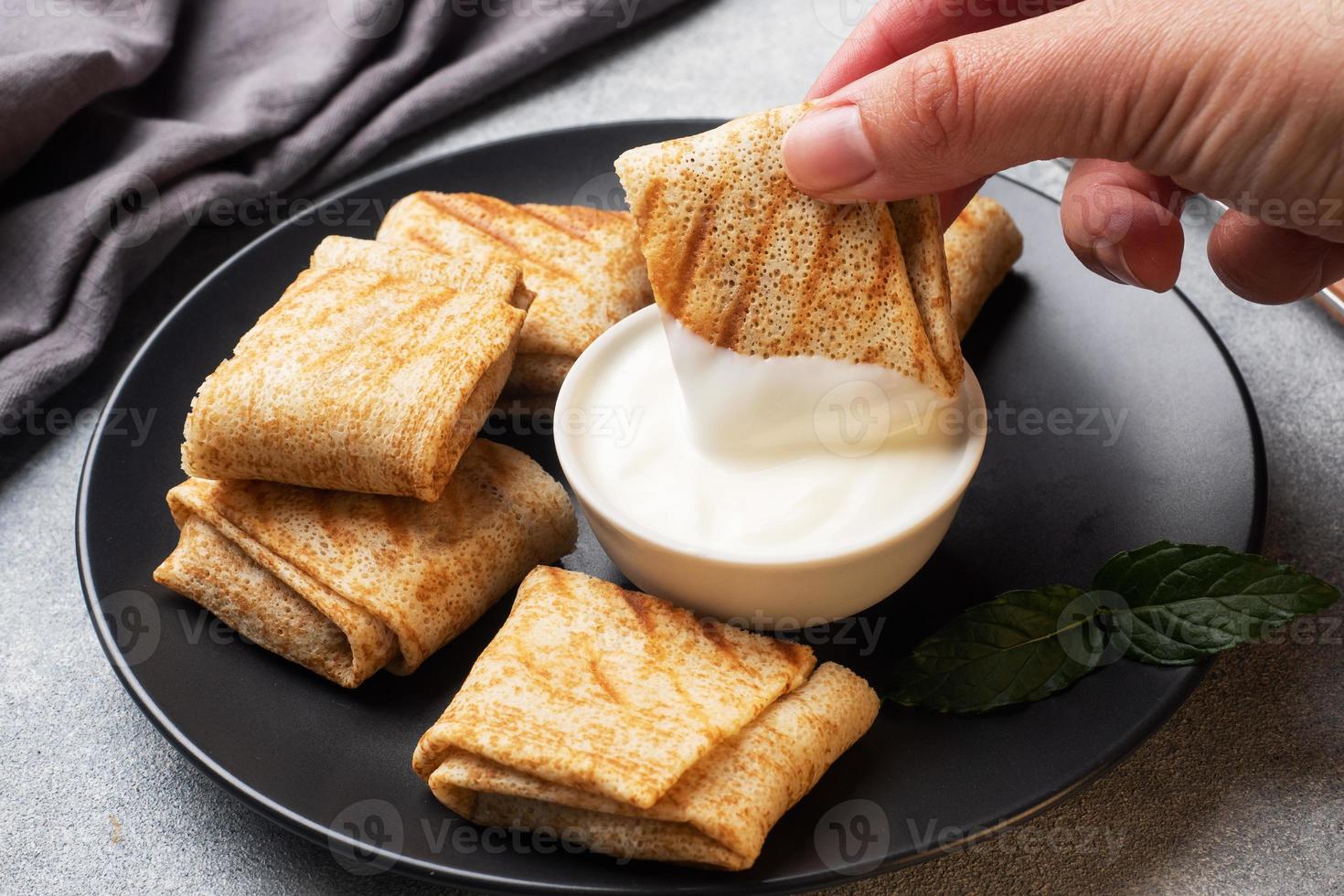Stuffed thin pancakes rolled into rolls are grilled on a black plate. Pancake roll is dipped in cream sauce. photo