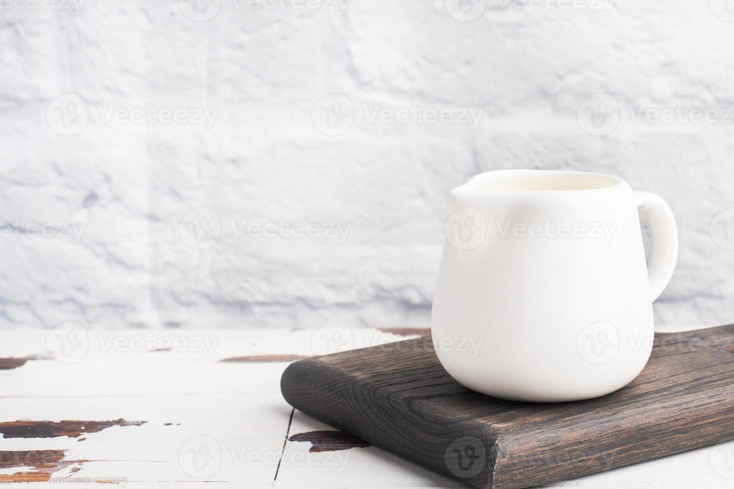 White ceramic milk jug with fresh milk on a gray background. Copy space. photo