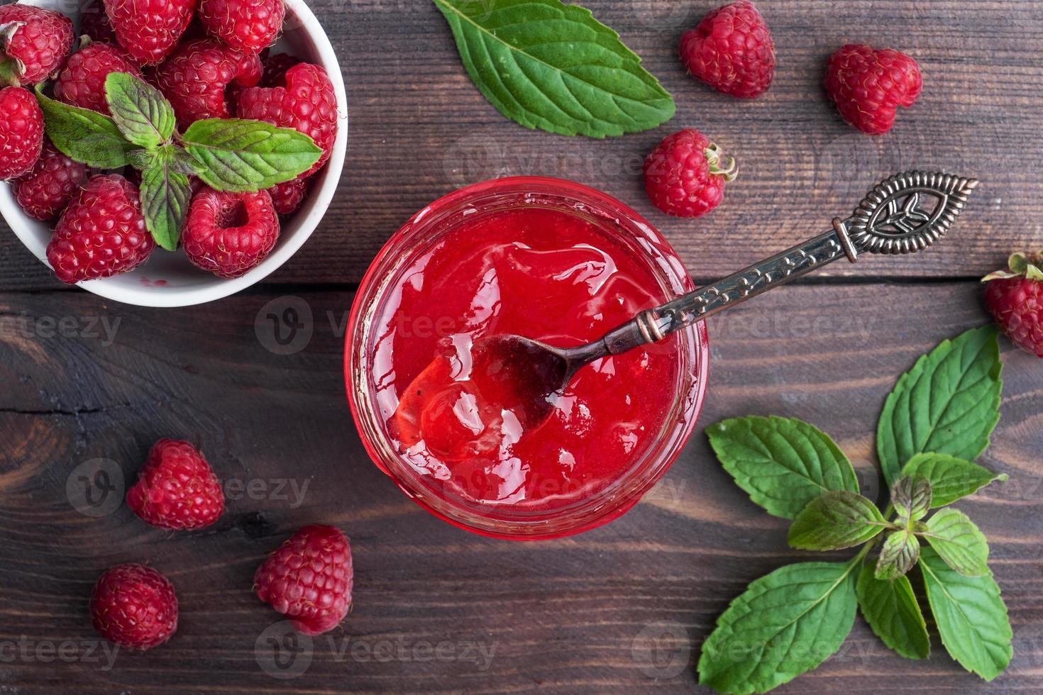 Homemade raspberry jam in a glass jar and fresh raspberries with mint on a wooden rustic background. Copy space photo
