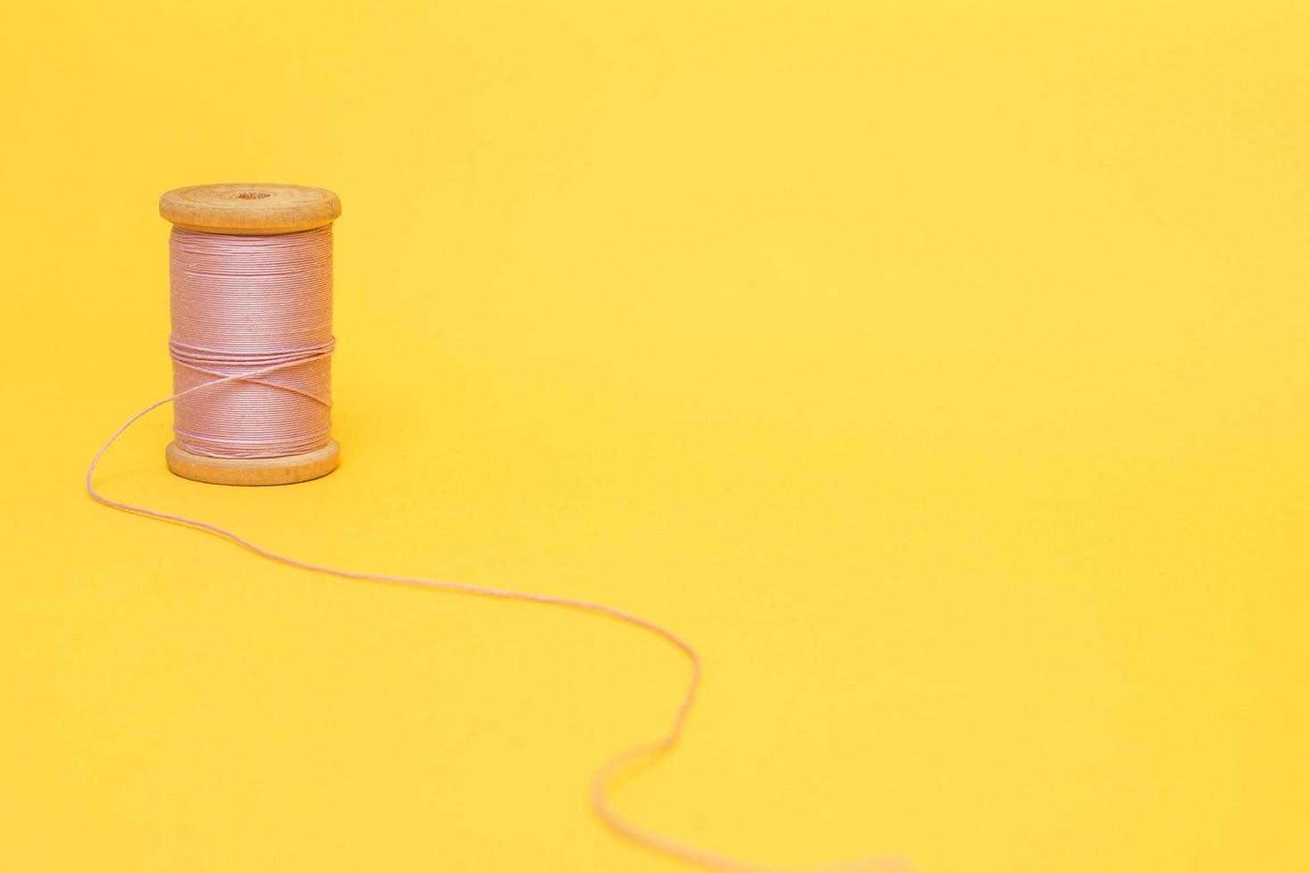 A spool of pink thread on a yellow background photo