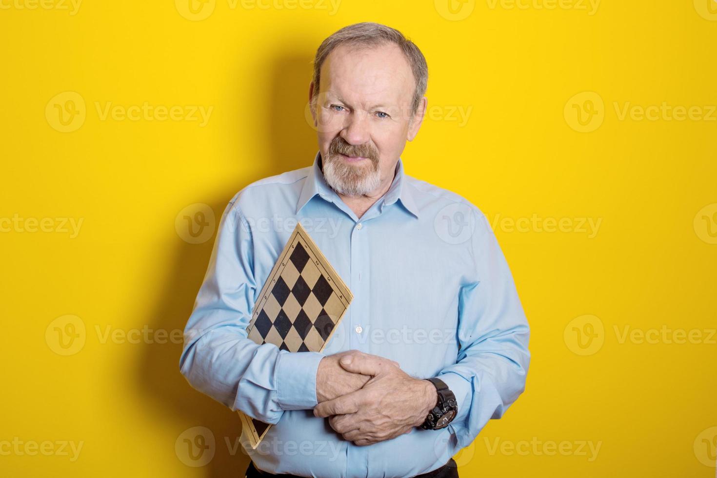 smiling elderly man holding checkers and chess board in his hands on yellow background photo