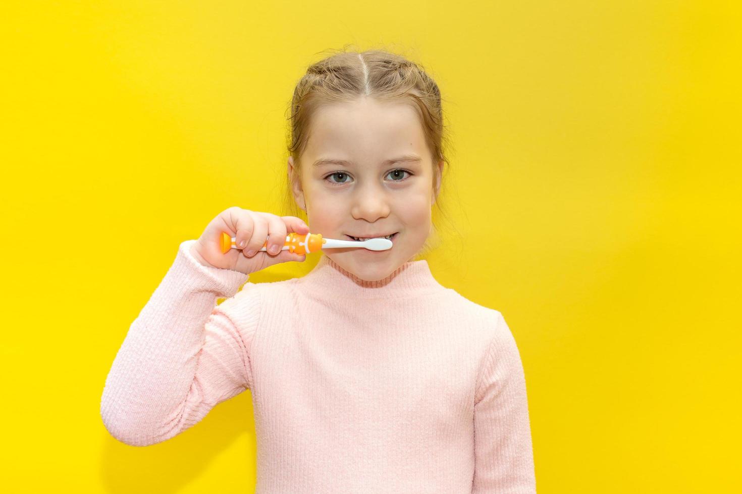 linda niña cepillándose los dientes con fondo amarillo. foto