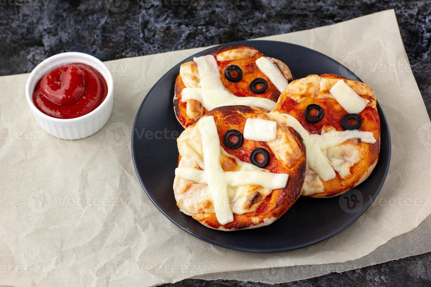 Mini pizza as mummy for kids with cheese, olives and ketchup. Funny crazy Halloween food for children. photo