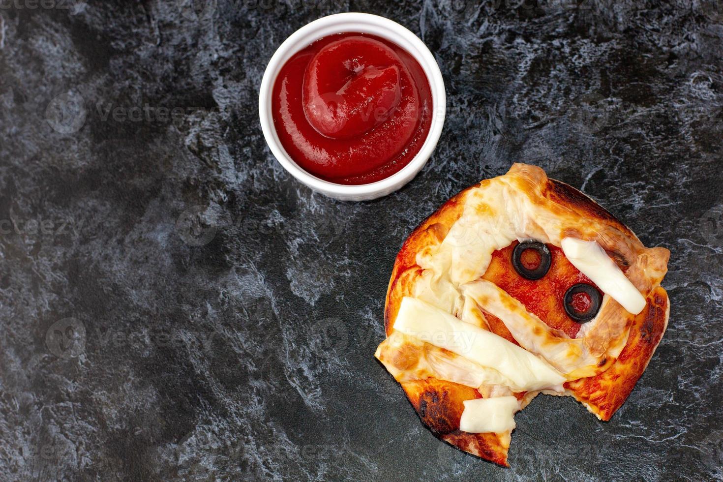 mini pizza como momia para niños con queso, aceitunas y ketchup. divertida comida loca de halloween para niños. foto
