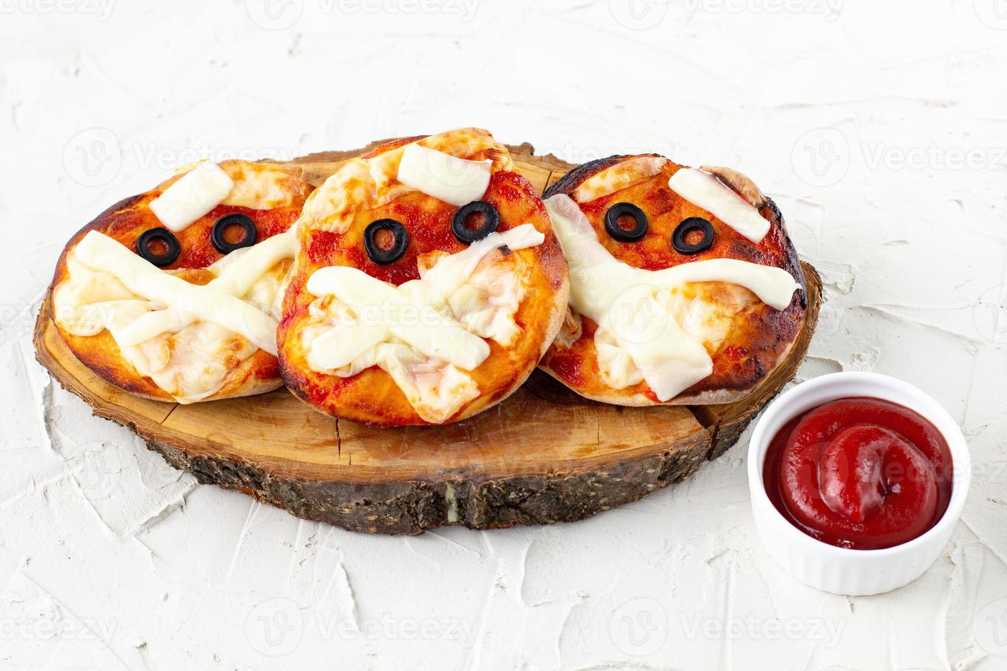 mini pizza como momia para niños con queso, aceitunas y ketchup. divertida comida loca de halloween para niños foto