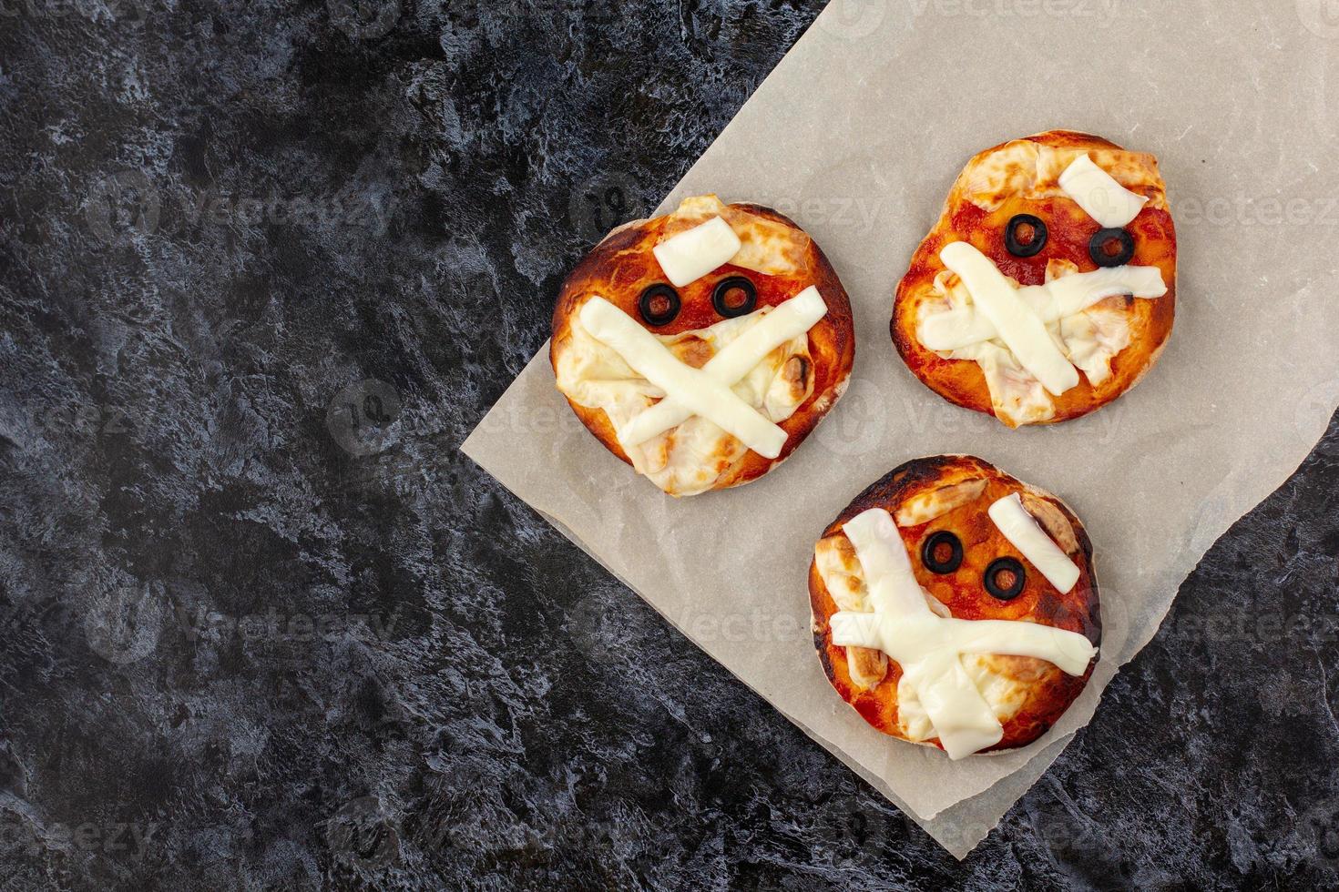 mini pizza como momia para niños con queso, aceitunas y ketchup. divertida comida loca de halloween para niños. foto