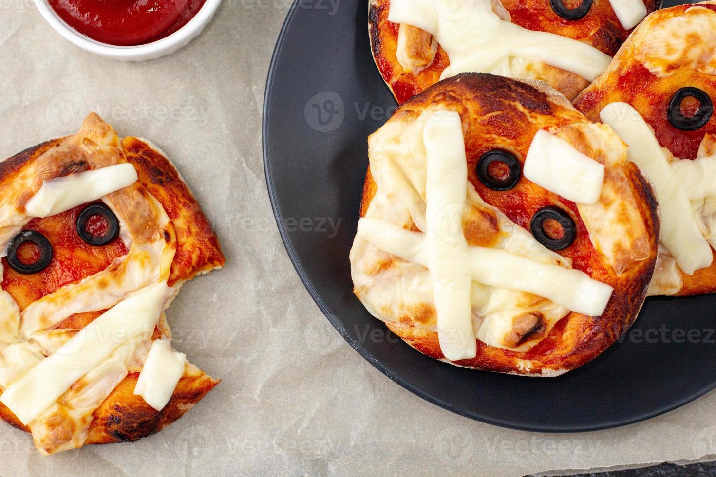 mini pizza como momia para niños con queso, aceitunas y ketchup. divertida comida loca de halloween para niños. foto