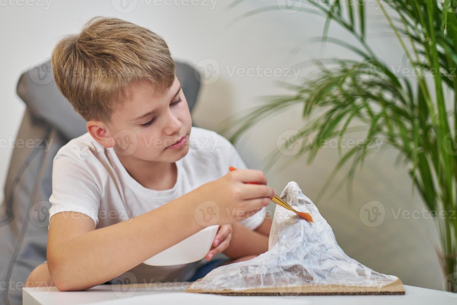 Schoolboy makes creative project in form of papier mache mountain. photo