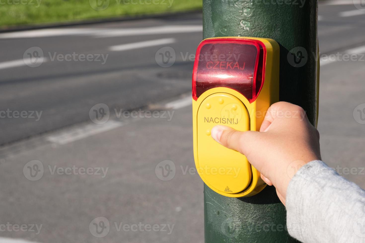 Child hand presses a yellow device with a button on demand on traffic light photo