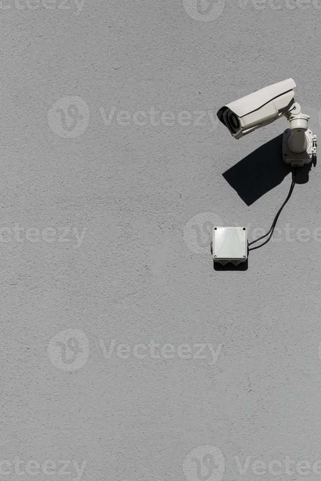 small white surveillance camera on flat gray matte plaster wall photo