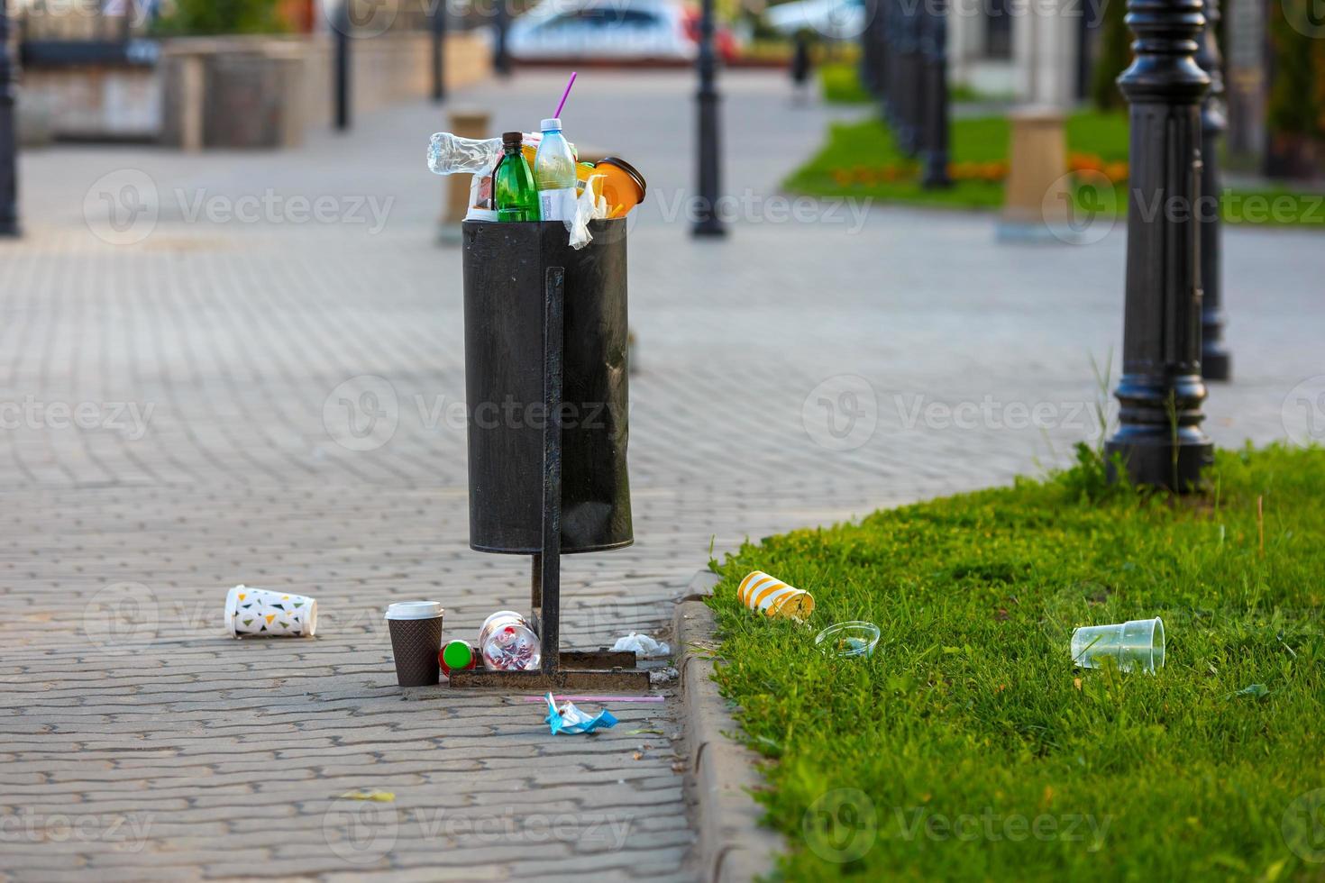 overflowing trash can on the sidewalk pavement at summer daylight photo