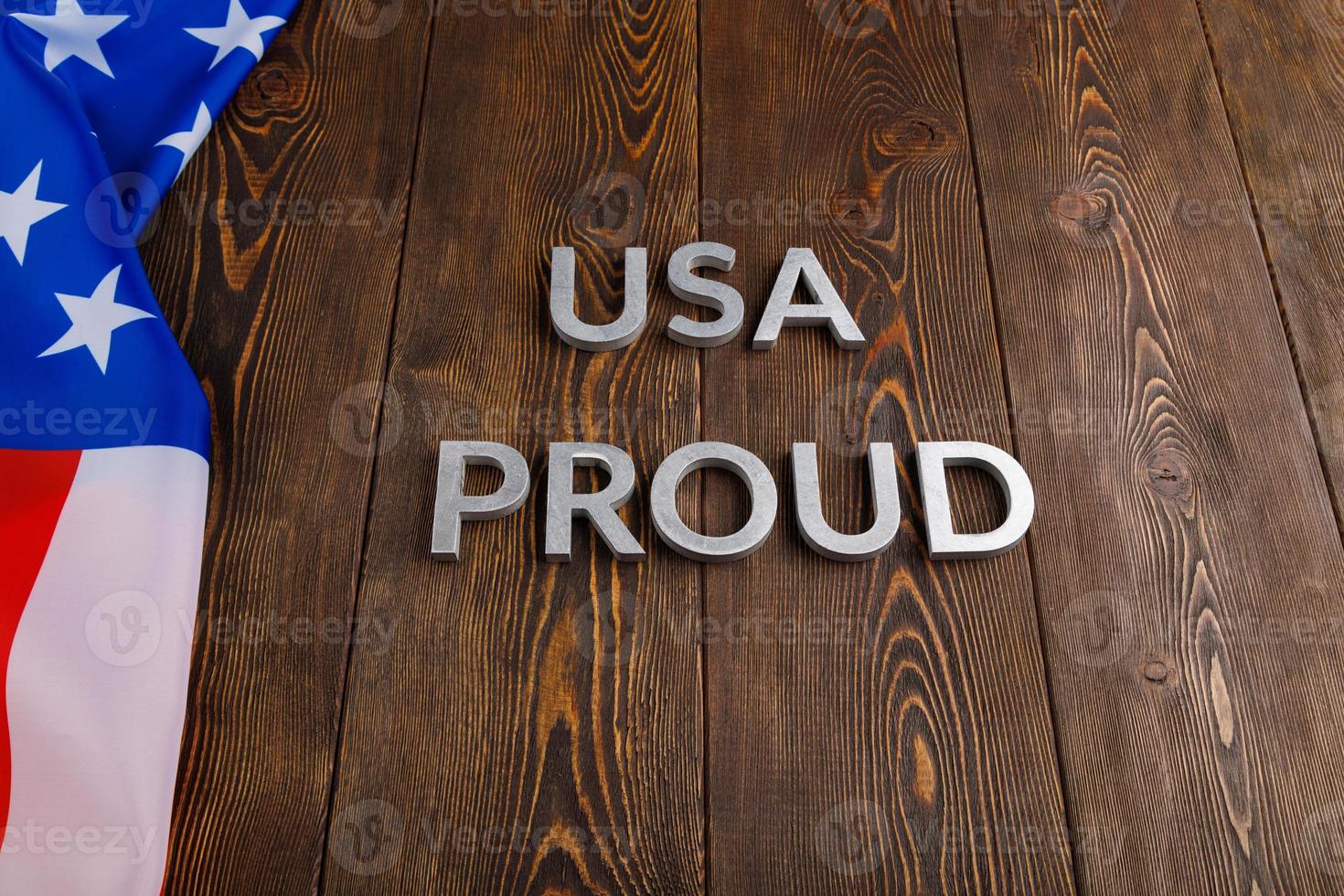 words USA proud laid with silver metal letters on brown wooden surface with flag of United States of America photo