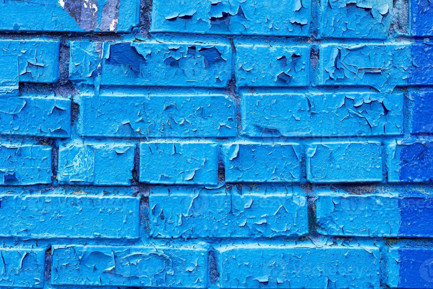 photo of the texture of a brick wall painted with blue paint, the paint is cracked and peeling off in flakes