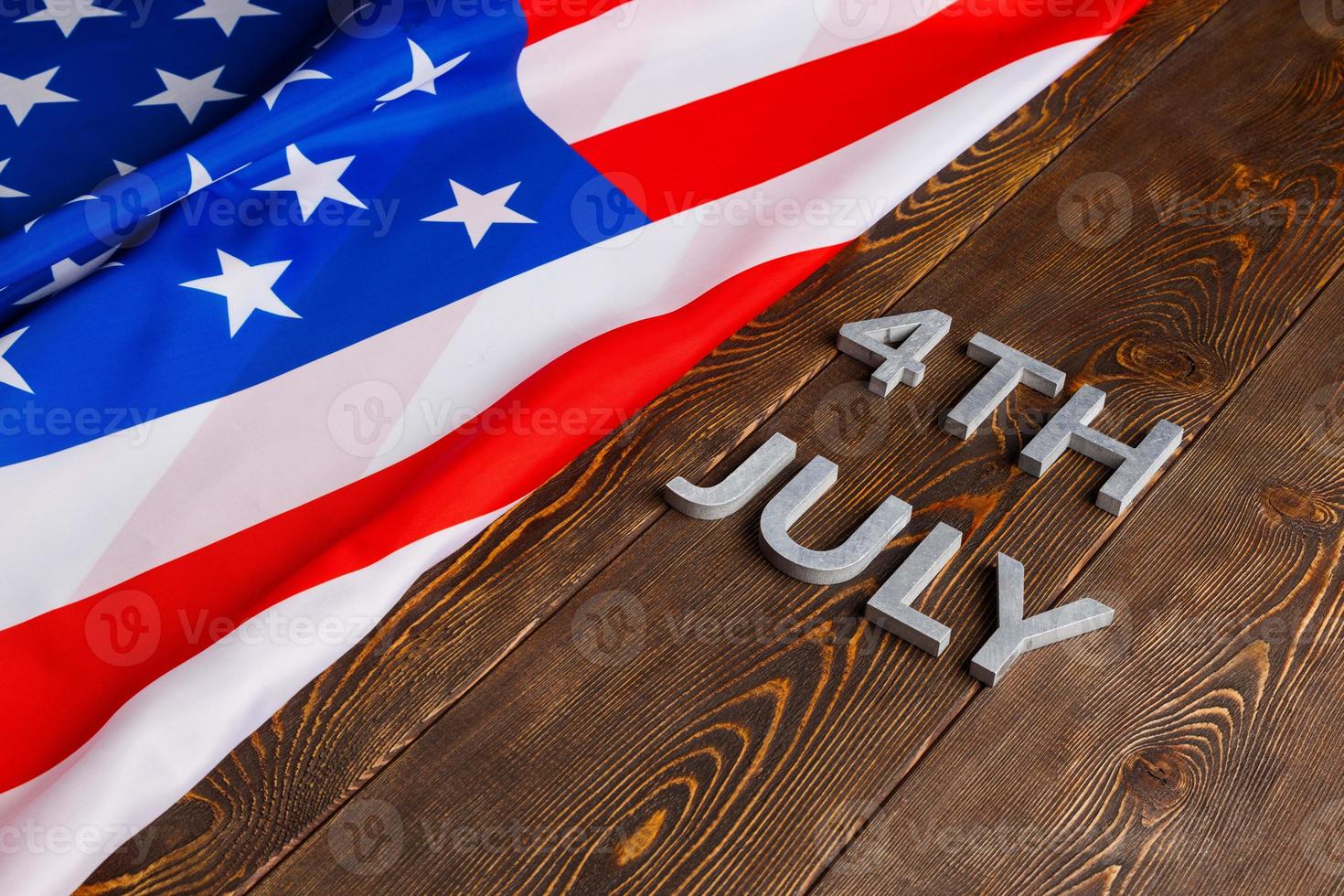 the words 4th july and crumpled usa flag on flat textured wooden surface background photo