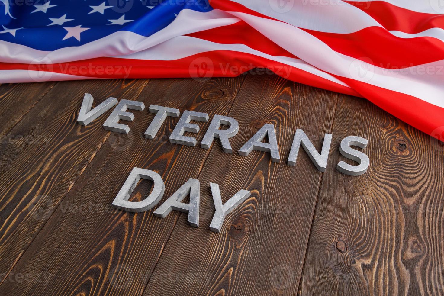 the words veterans day laid with silver metal letters on wooden board surface with crumpled usa flag at right side with diagonal perspective photo