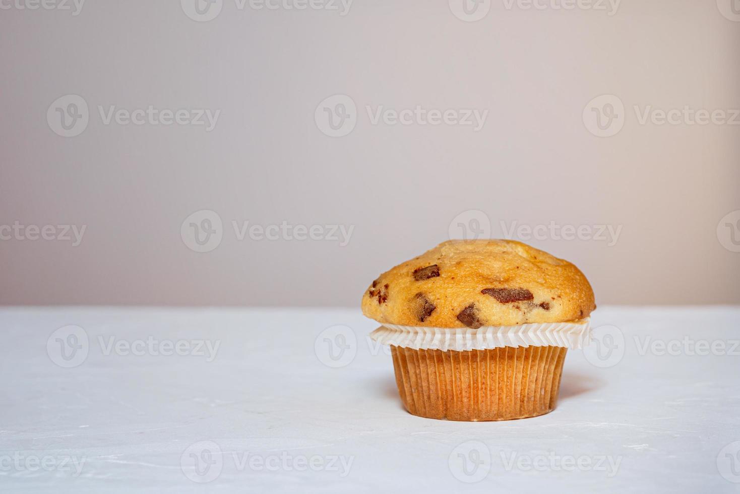 One muffin with chocolate peices on a white table photo