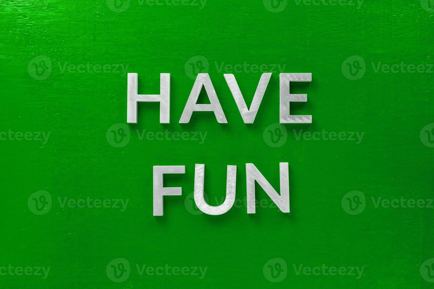 the words have fun laid with silver metal characters on green background in central flat lay composition photo
