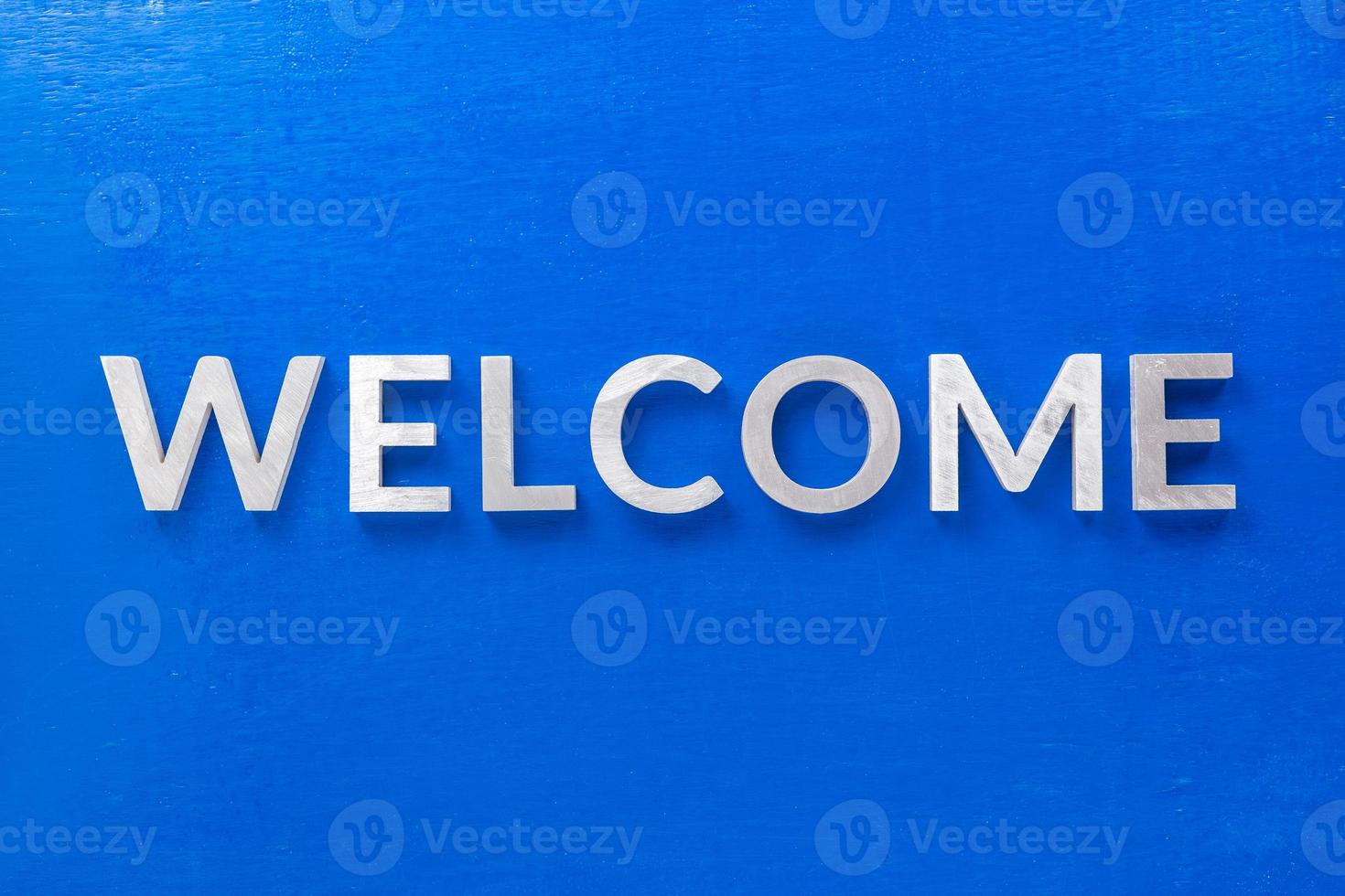 the word welcome laid with silver metal characters on blue painted wooden board in flat lay with central composition photo