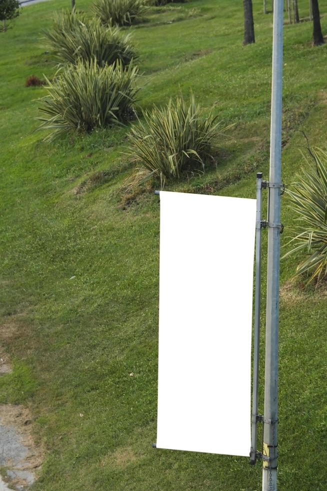 Empty vertical cloth banner on a street lamp and blurred garden background photo