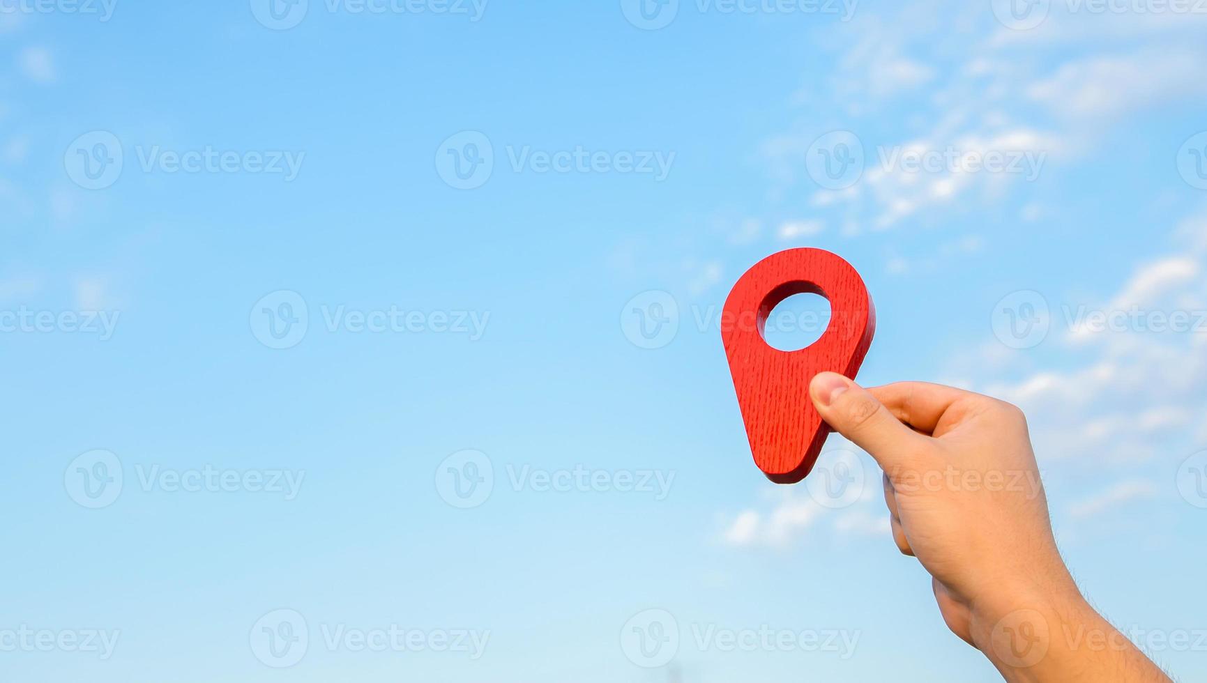 Red location pin in hand on sky background. The concept of location and orientation in space. Cartography. Tourism and travel. Land and real estate market. Air transportation and house moving. photo