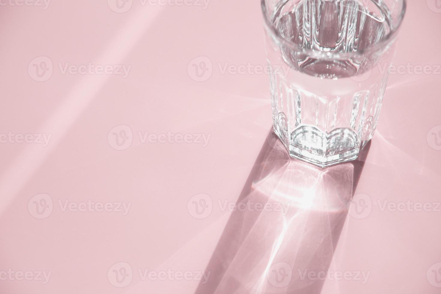 Glass of water on pink, sunlight and shadow, copy space photo