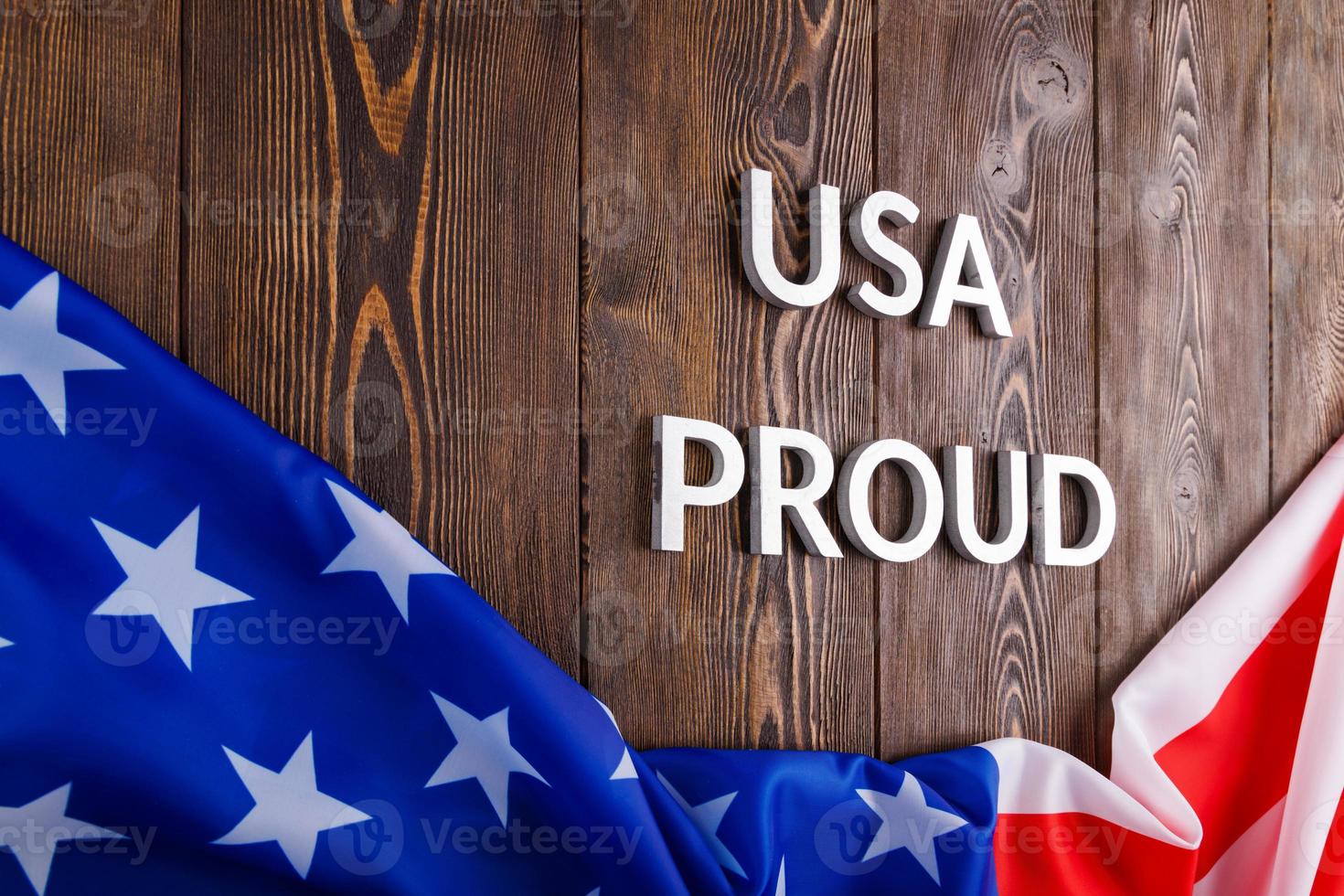 words USA proud laid with silver metal letters on brown wooden surface with flag of United States of America photo