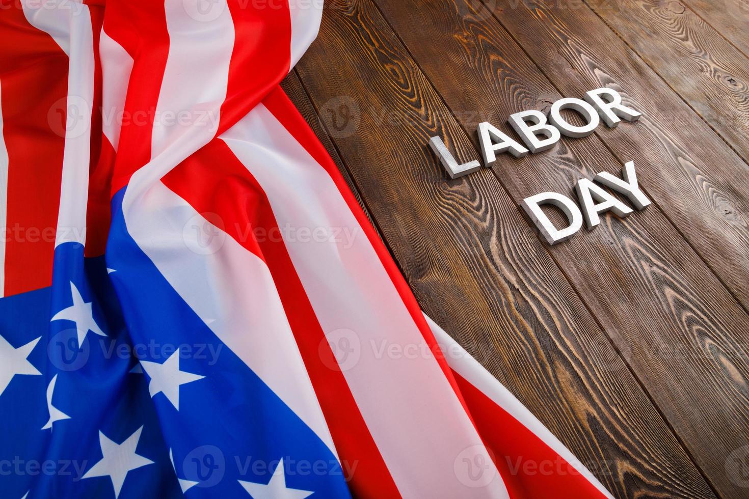 words labor day laid with silver metal letters on wooden surface with crumpled USA flag on left side photo