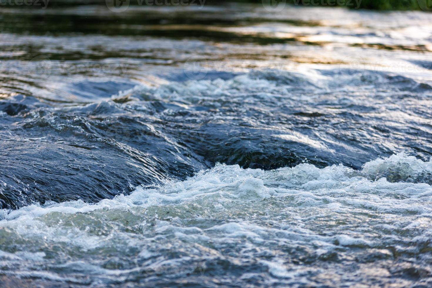 agua que fluye de un río de verano con una pequeña cascada rápida a la luz del atardecer foto