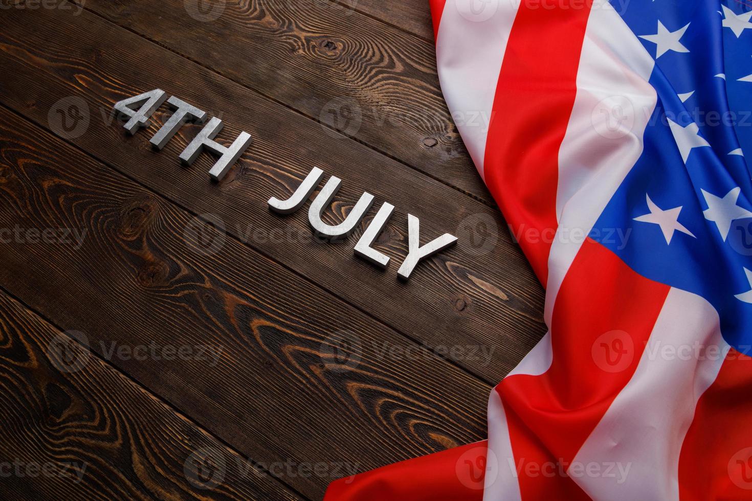 the words 4th July and crumpled USA flag on flat textured wooden surface background photo