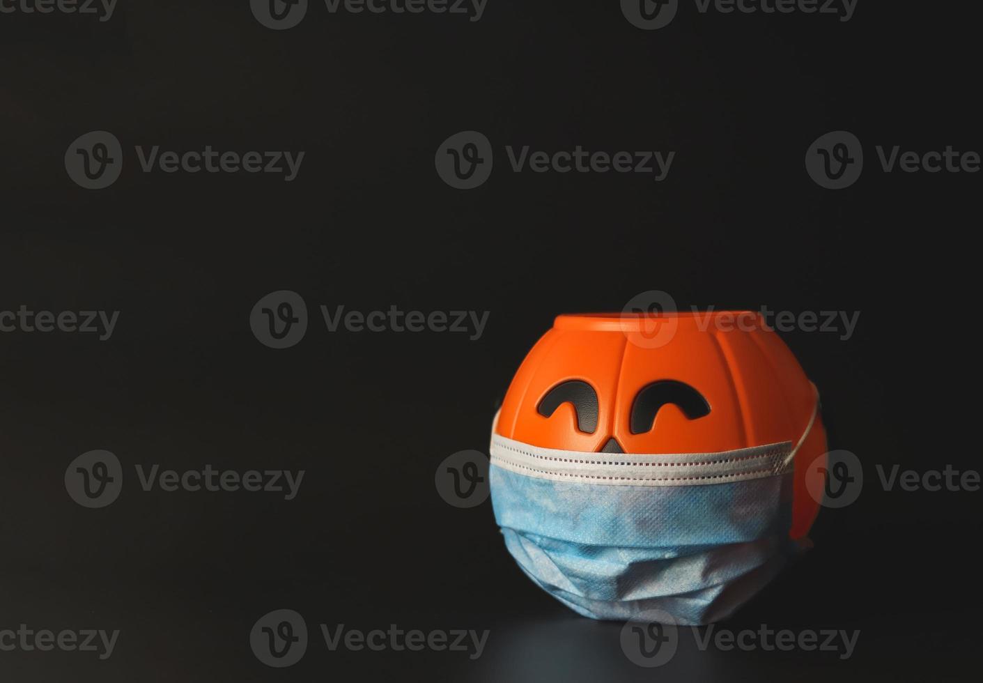 plastic halloween pumpkin wearing medical face mask  on black background with copy space. New normal  halloween concept photo