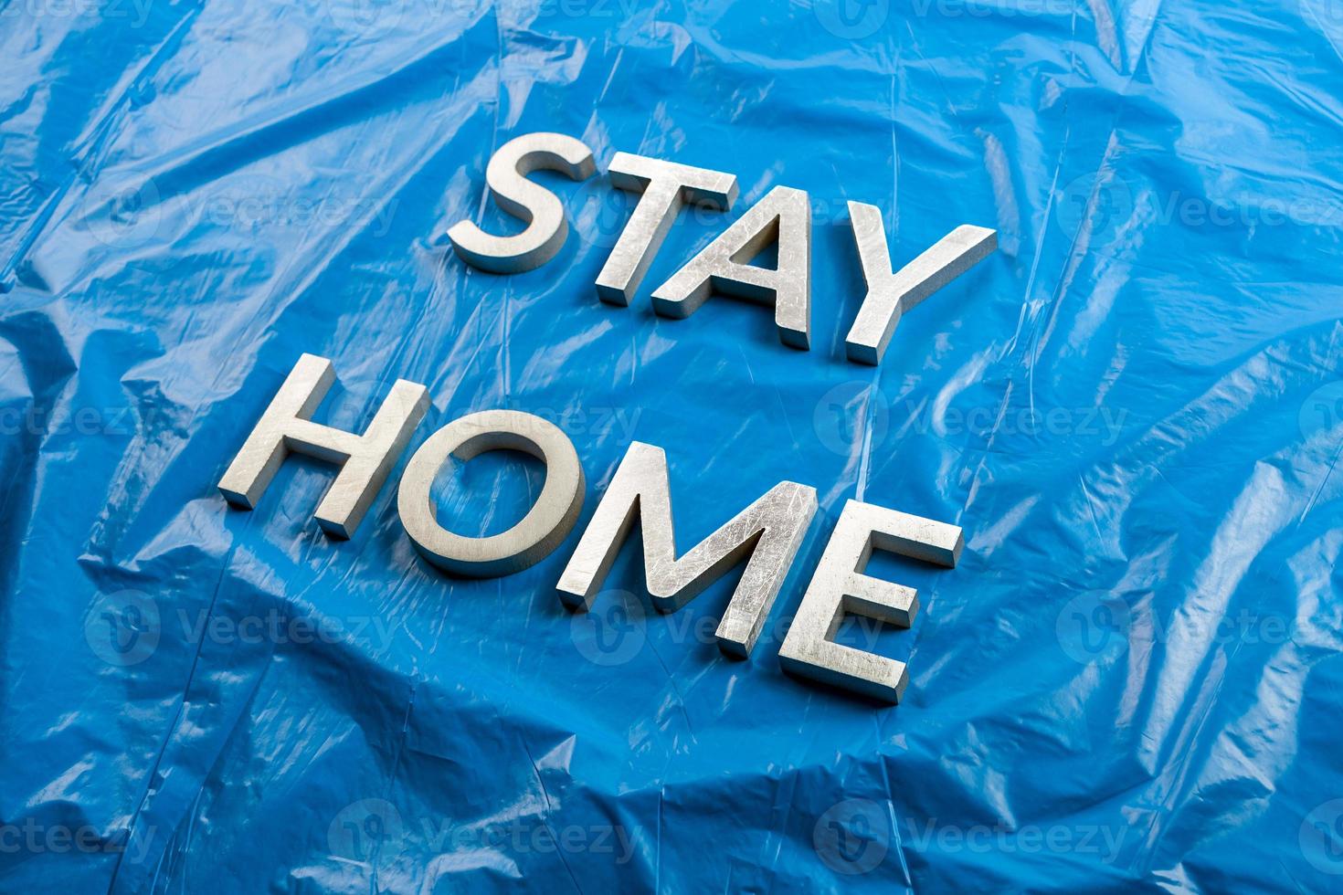 the words stay home laid with silver metal letters on crumpled blue plastic background in slanted diagonal perspective photo