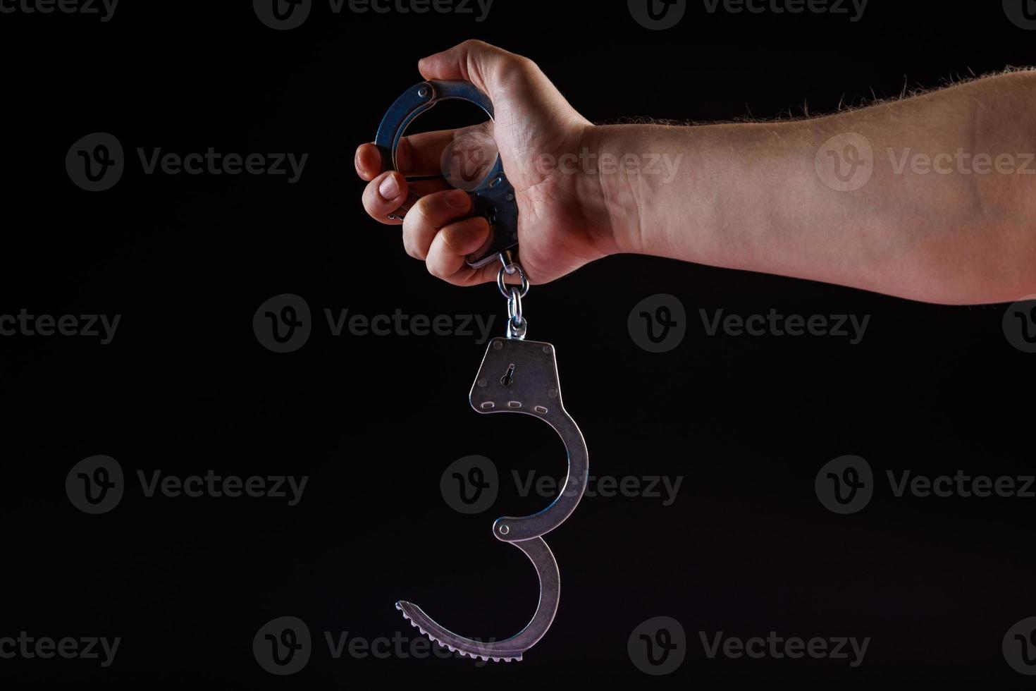 bare caucasian hand holding opened silver steel handcuffs on black background photo