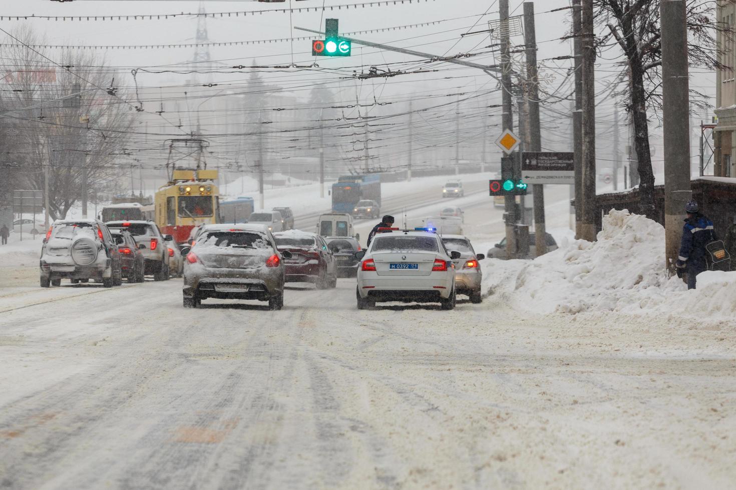 Tula, Russia  February 13, 2020 City cars stopped at crossroads in front of traffic lights with police vehicle during heavy snowfall. photo