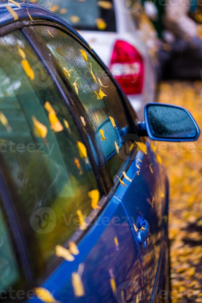 lado del coche azul húmedo con hojas de otoño y enfoque selectivo foto