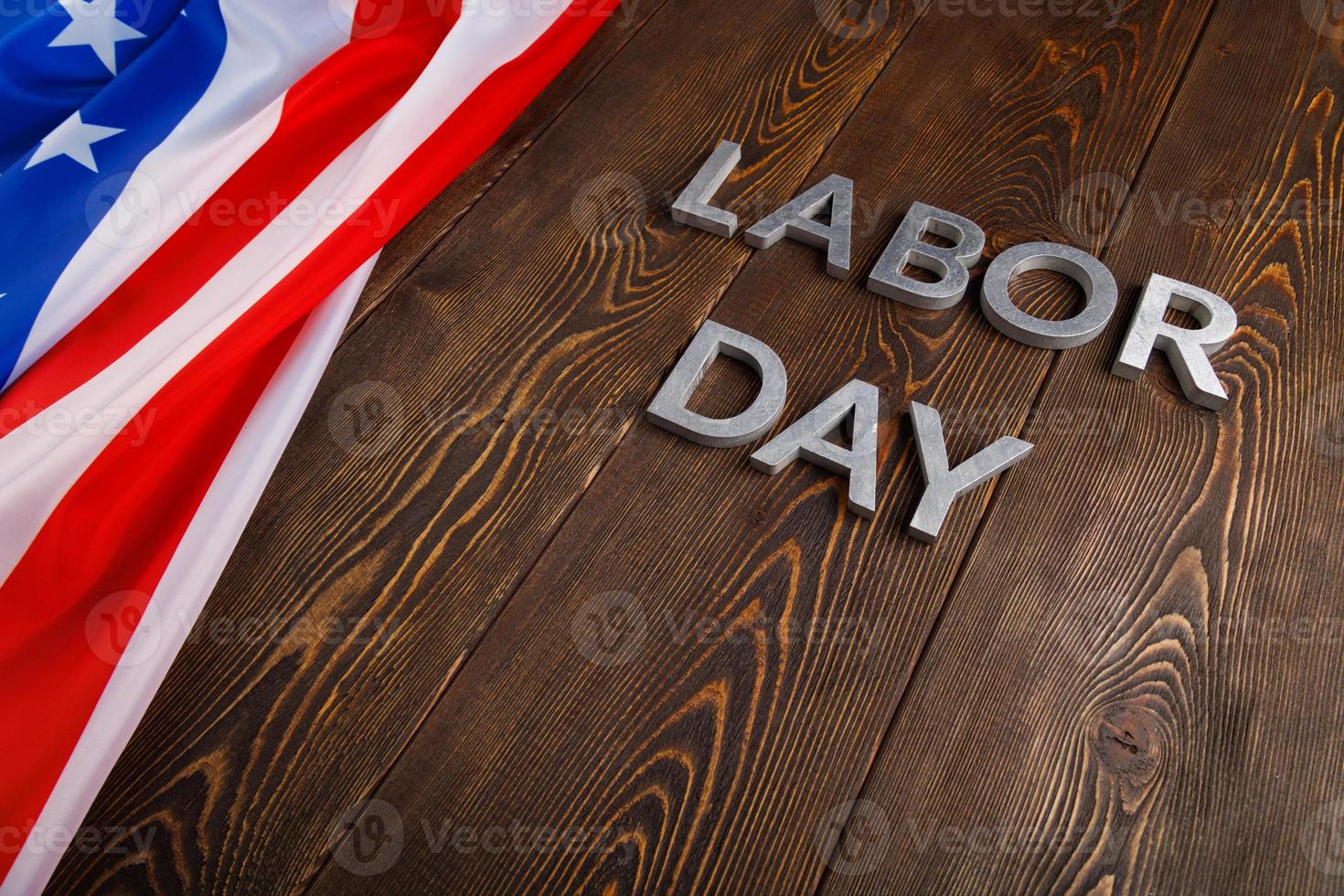words labor day laid with silver metal letters on wooden surface with crumpled USA flag on left side photo