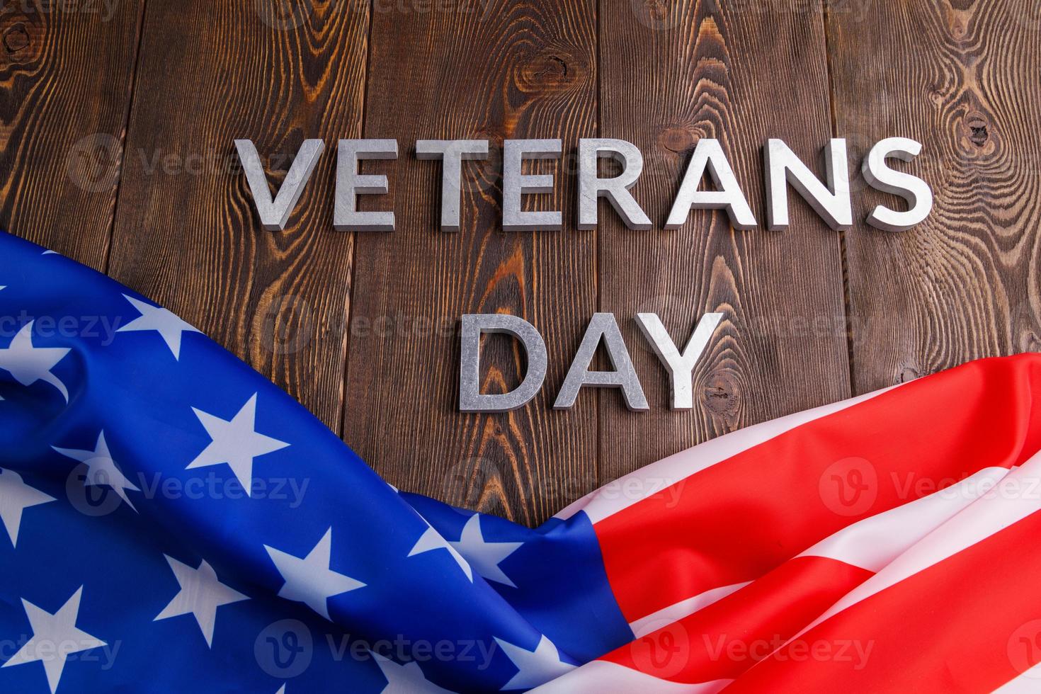 the words veterans day laid with silver metal letters on wooden board surface with crumpled usa flag photo