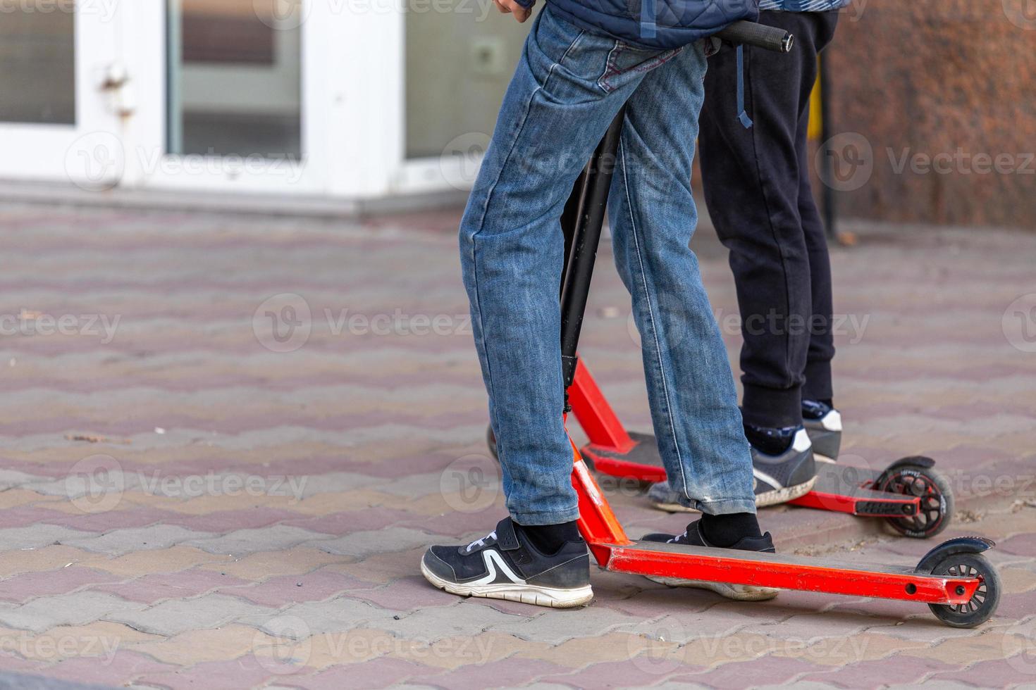 slim kids legs with scooters on the urban pavement sidewalk - closeup witn selective focus photo
