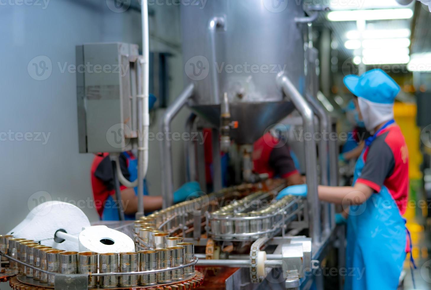 Canned fish factory. Food industry.  Sardines in red tomato sauce in tinned cans on conveyor belt at food factory. Blur workers working in food processing production line. Food manufacturing industry. photo