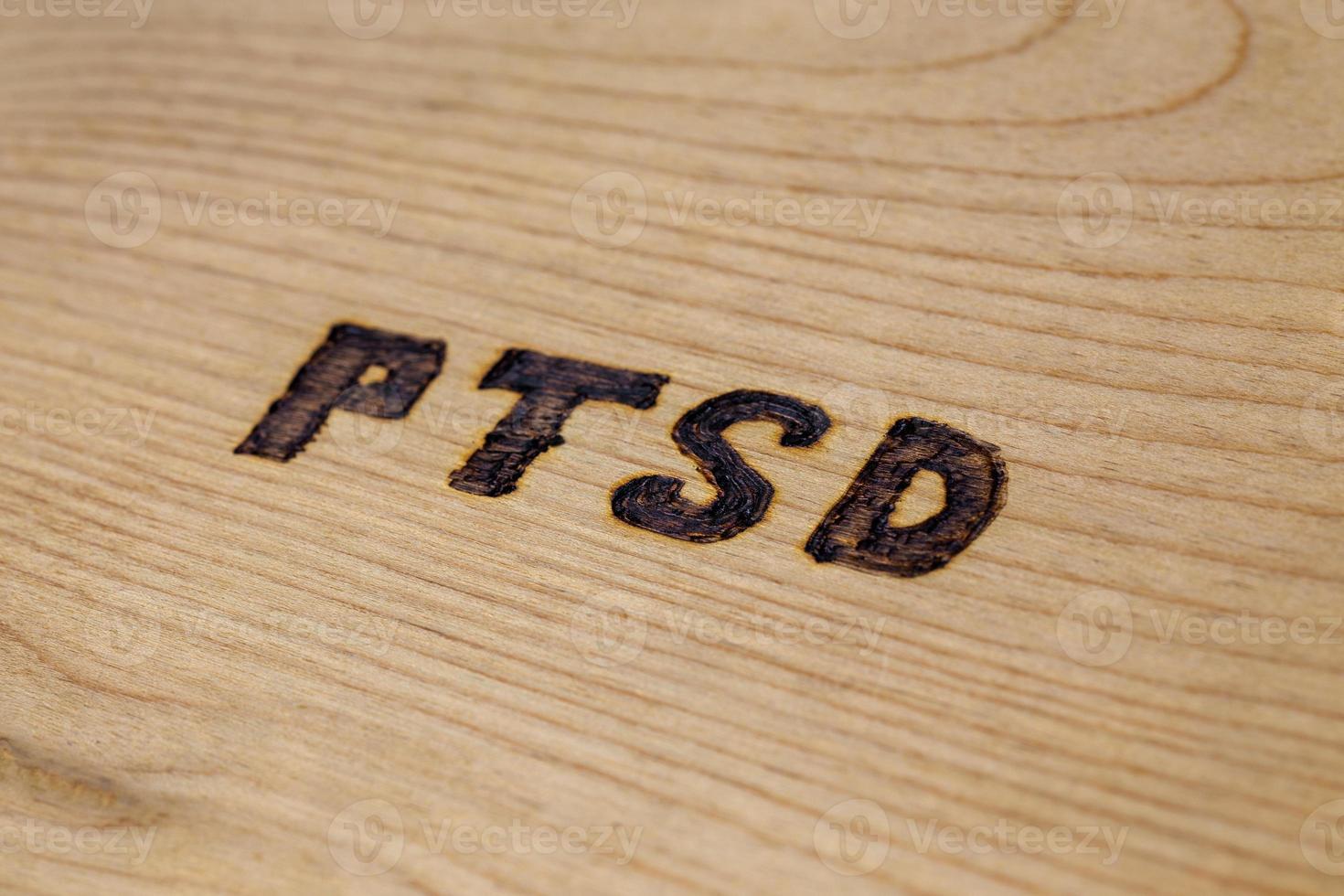 an abbreviation PTSD - post traumatic stress disorder - burned by hand on flat wooden board in diagonal composition photo