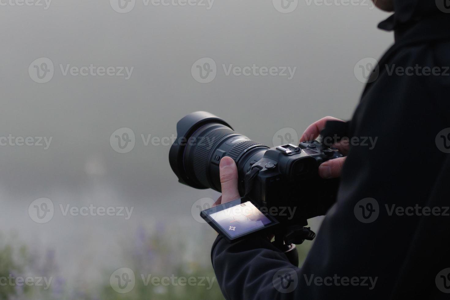 unrecognizable photographer shooting misty outdoor scene with contemporary black digital camera on a tripod with flip screen photo