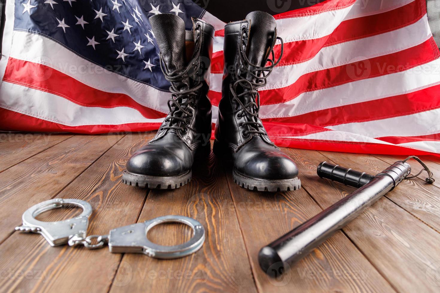 silver handcuffs, boots and police nightstick near US flag on wooden surface photo