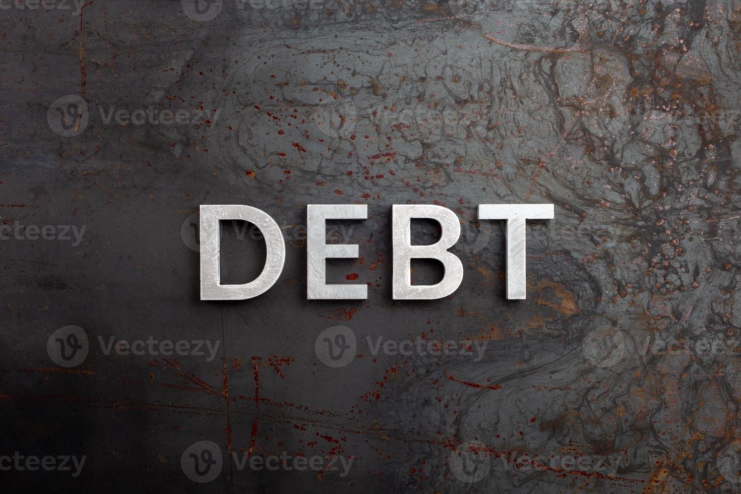 the word debt laid with silver letters on raw rusted steel sheet surface in flat lay perspective photo