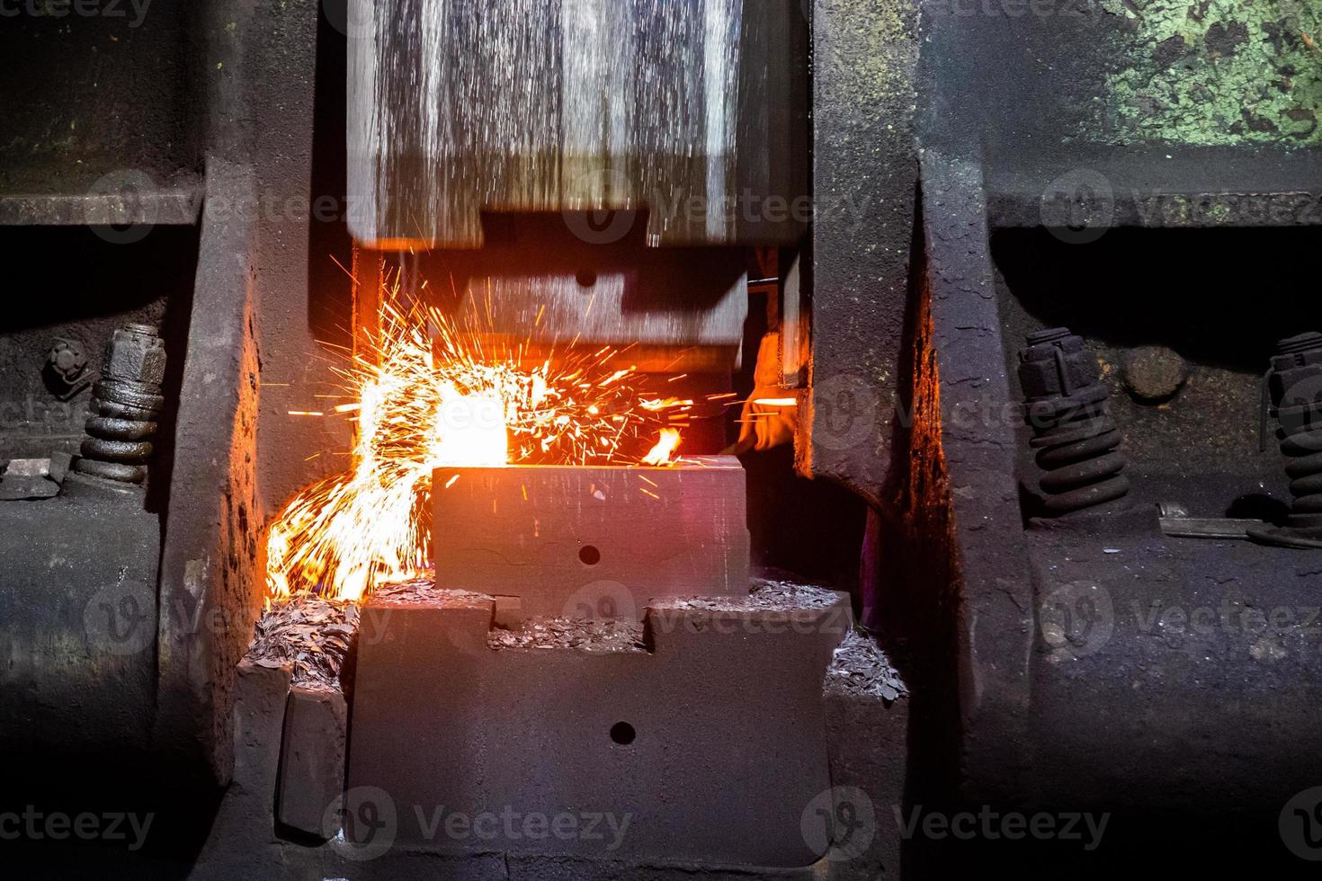 vista frontal de primer plano del proceso de forja de acero caliente con una gran máquina de martillos mecánicos foto