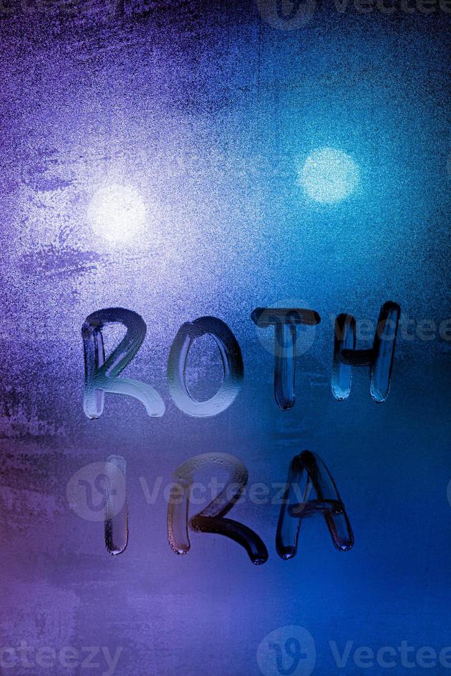 the words roth ira handwritten on night wet window glass surface photo