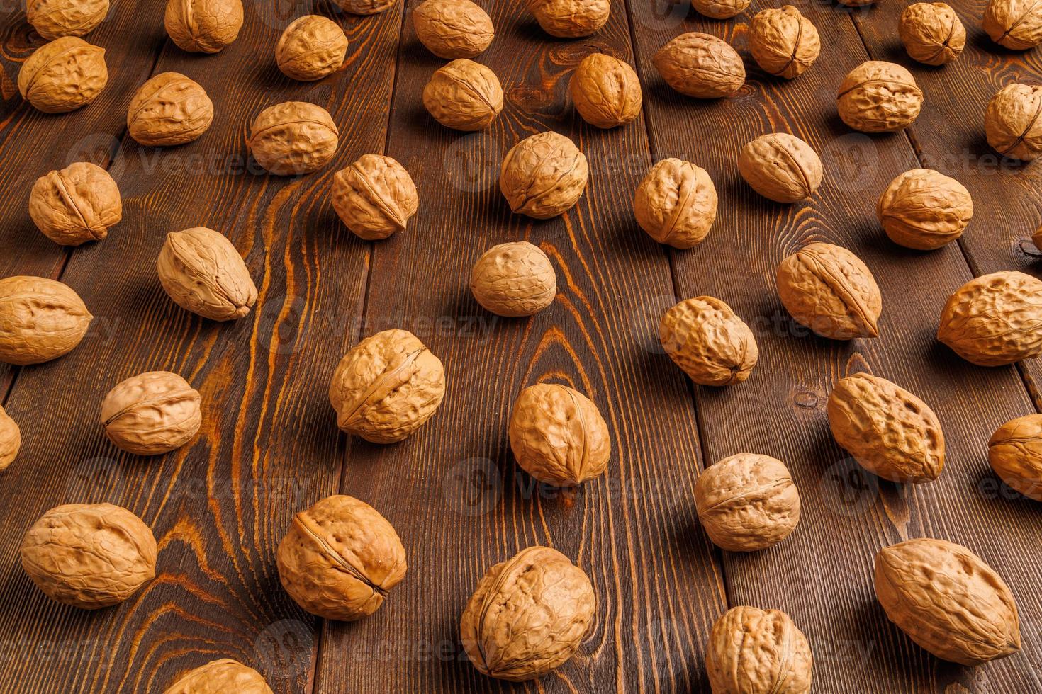 many walnuts with shells evenly spread out on brown wooden surface photo