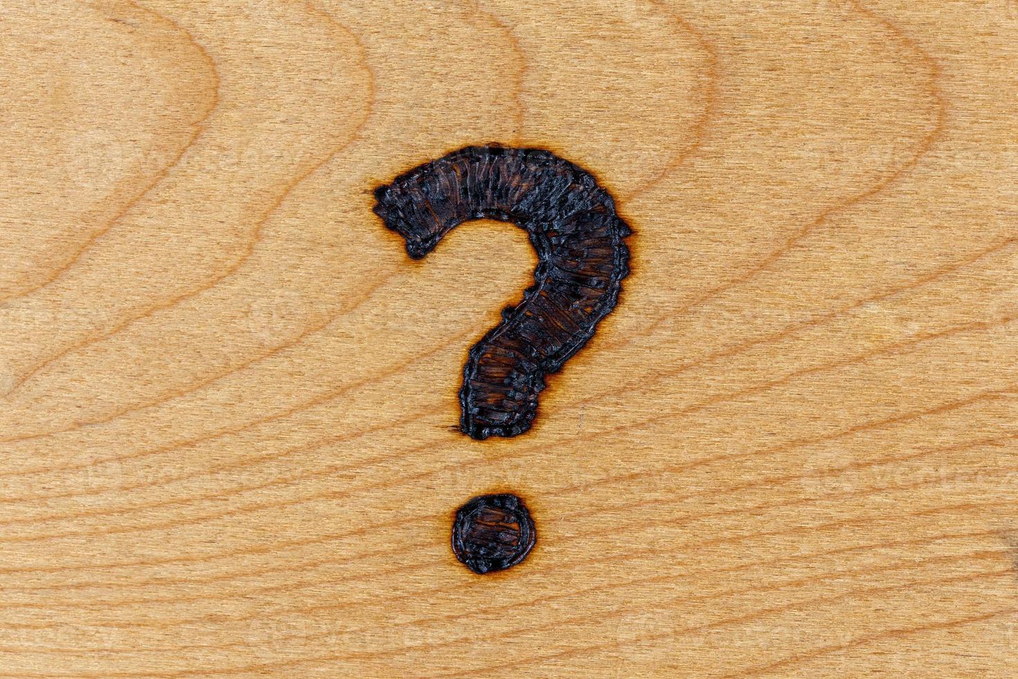 question mark drawn with handheld woodburner on bright flat wooden surface photo