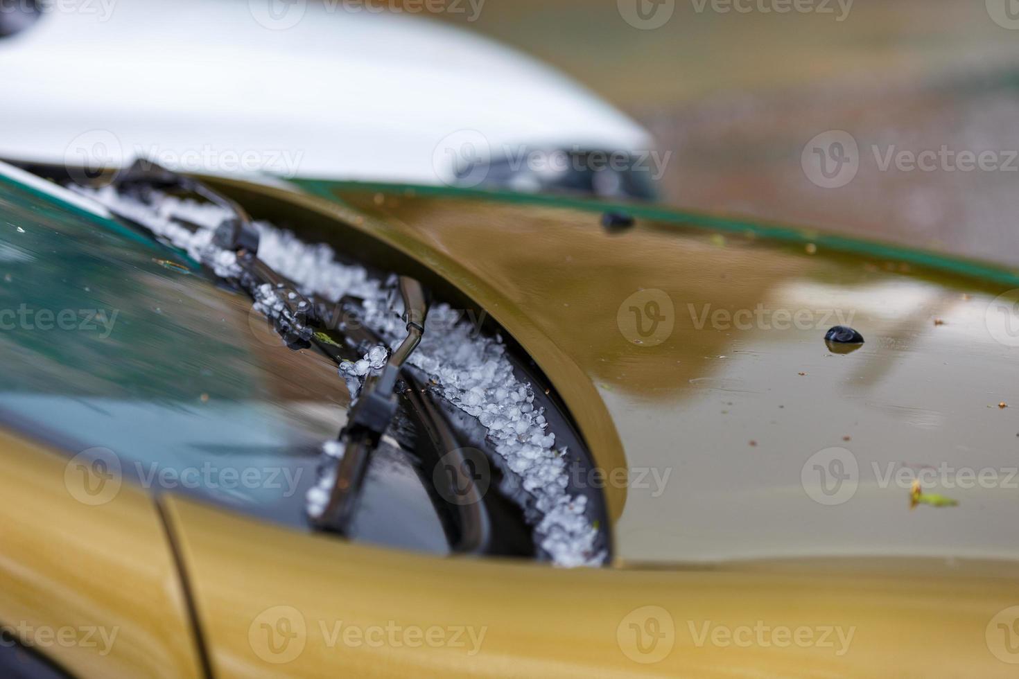 pequeñas bolas de hielo de granizo en el capó amarillo del coche después de una fuerte tormenta de verano foto