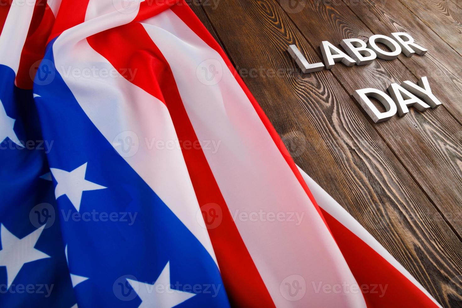 palabras día del trabajo colocadas con letras de metal plateado en una superficie de madera con una bandera de estados unidos arrugada en el lado izquierdo foto