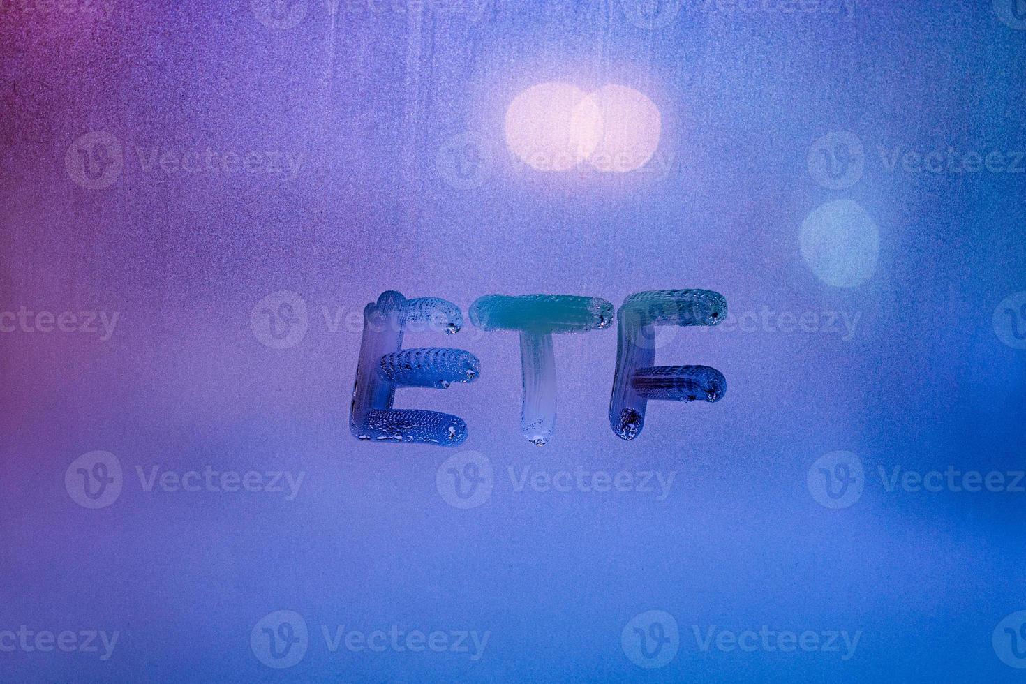 abbreviation word etf - exchange traded funds - handwritten on foggy glass window at night with neon blue back street light photo