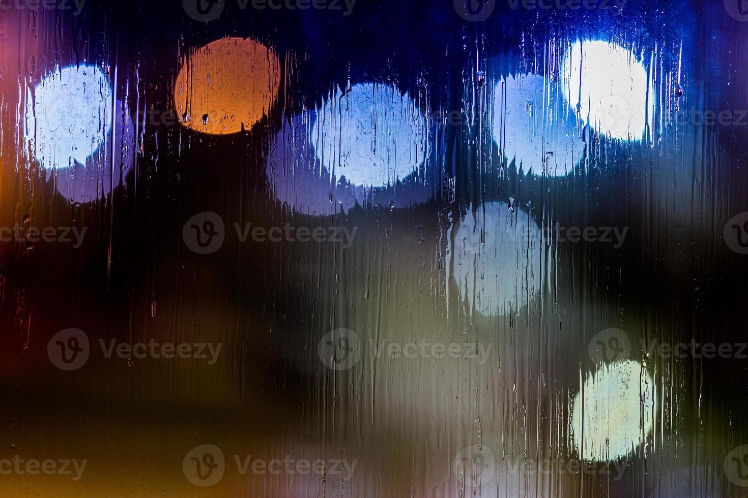 an abstract background night street lights bokeh through wet glass, close-up with selective focus photo